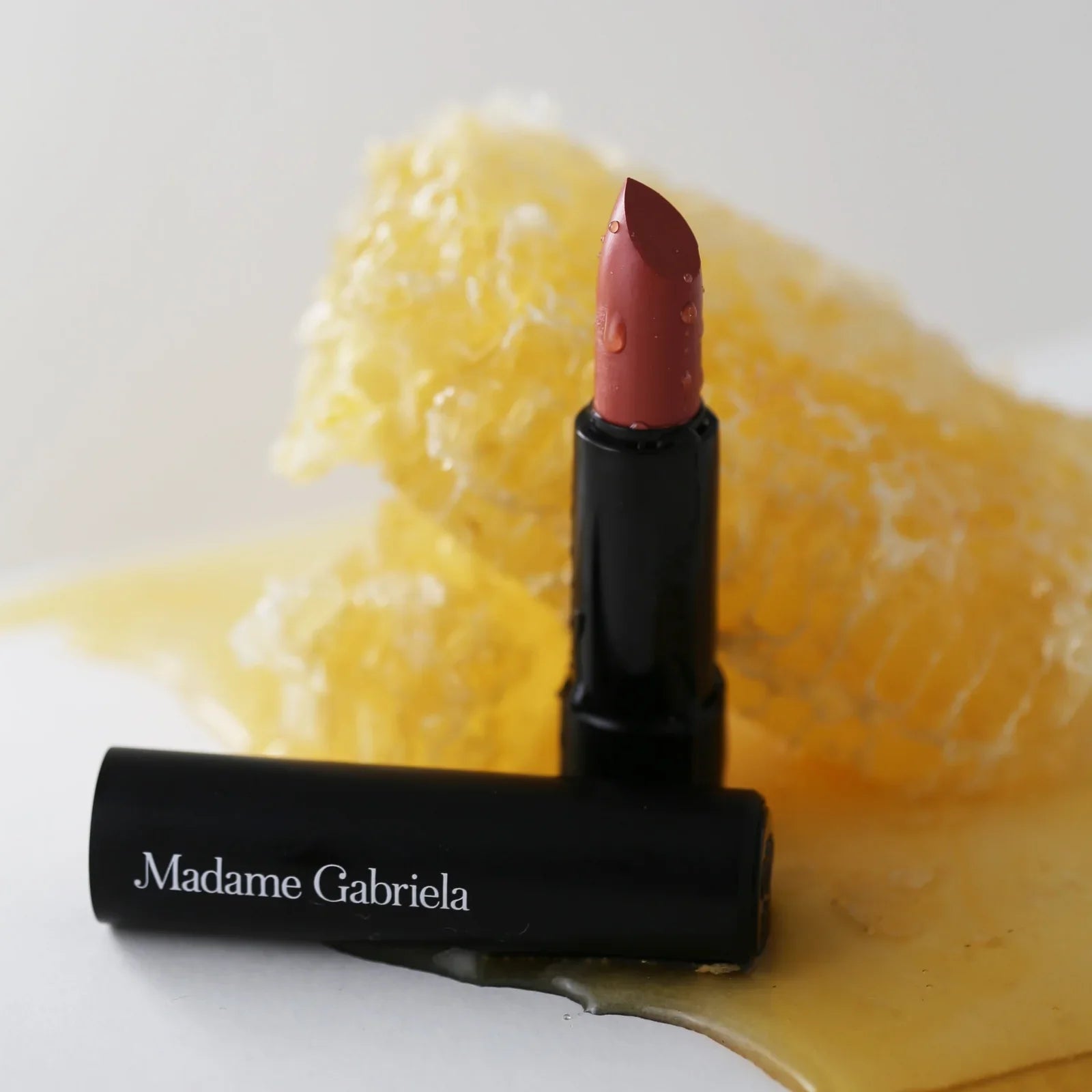 A tube of neutral pink Madame Gabriela Clean Beauty Lipstick placed in a pile of Mānuka honeycomb, highlighting its formulation.