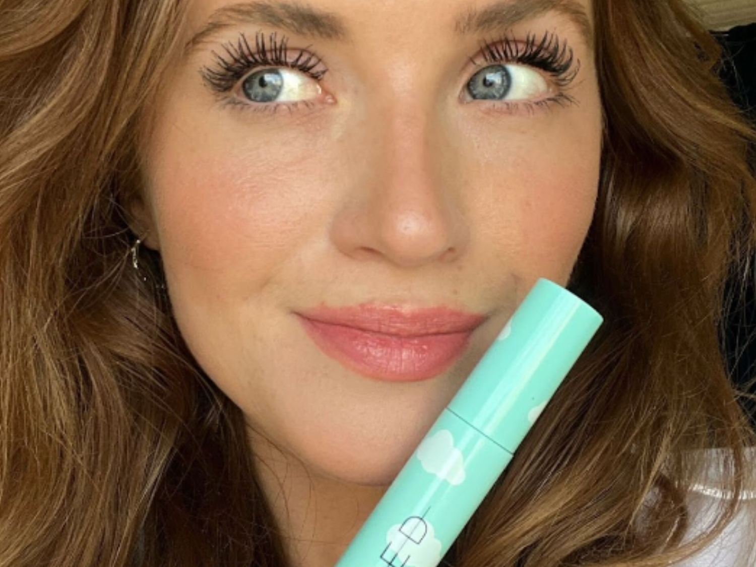A selfie of a woman holding SWEED Cloud Mascara, showing her long, defined lashes.