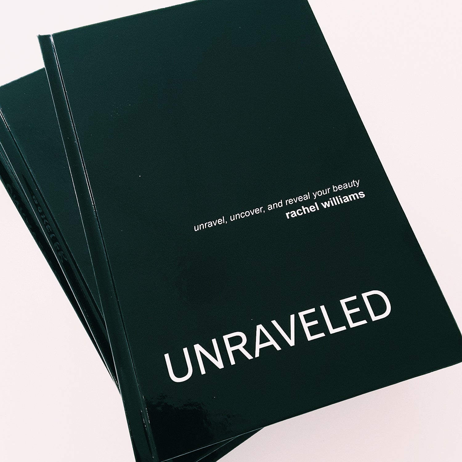 A stack of minimal black Unraveled books with capitalized white text by Rachel Williams of LORDE Beauty and Cosmetics.
