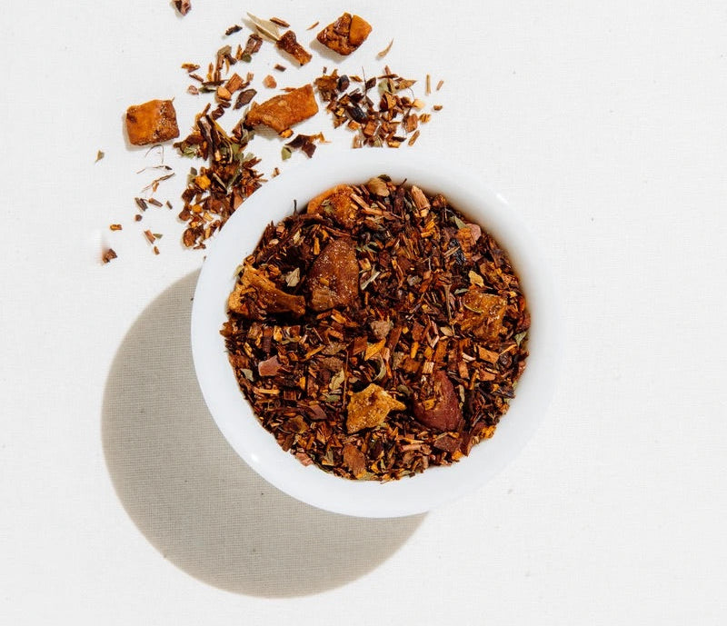 Loose leaf Art of Tea Apple Pie placed inside and scattered around a white cup in a well-lit room.