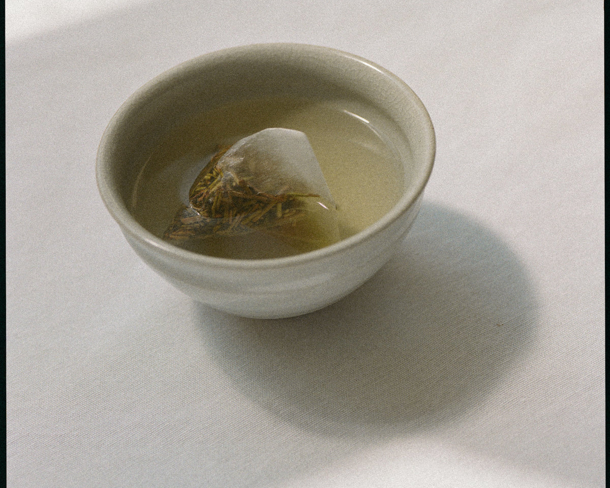 A small cup of green Tekuno Sencha Satsuki Tea placed in a well-lit room.