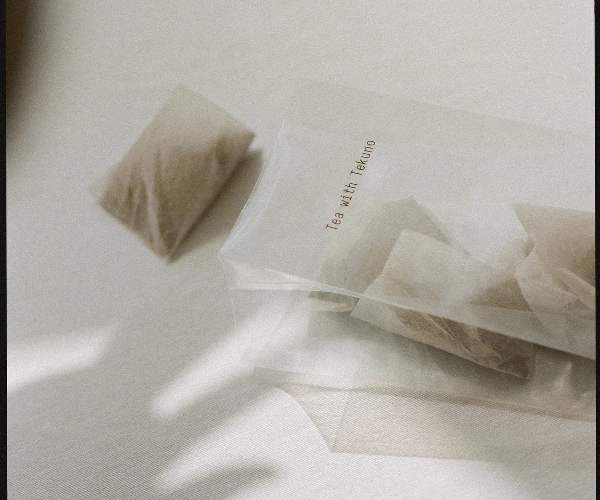 A clear cloth 'Tea with Tekuno' tea bag of Tekuno Sencha Satsuki Tea with small black branding text in a well-lit room.