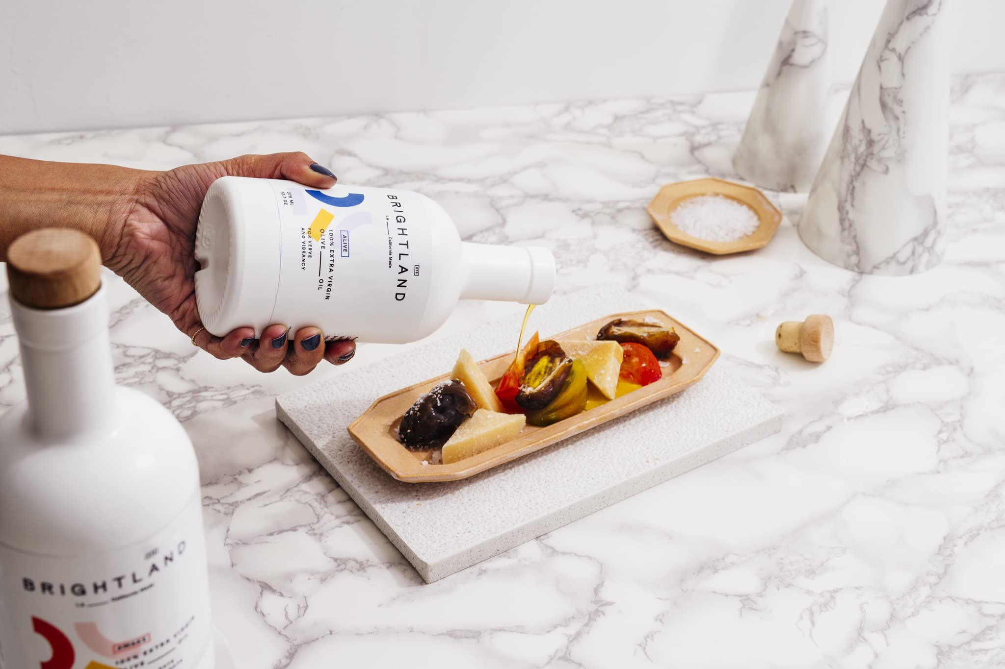 Brightland Cold Pressed Alive Olive Oil poured over a charcuterie platter on a marble table.