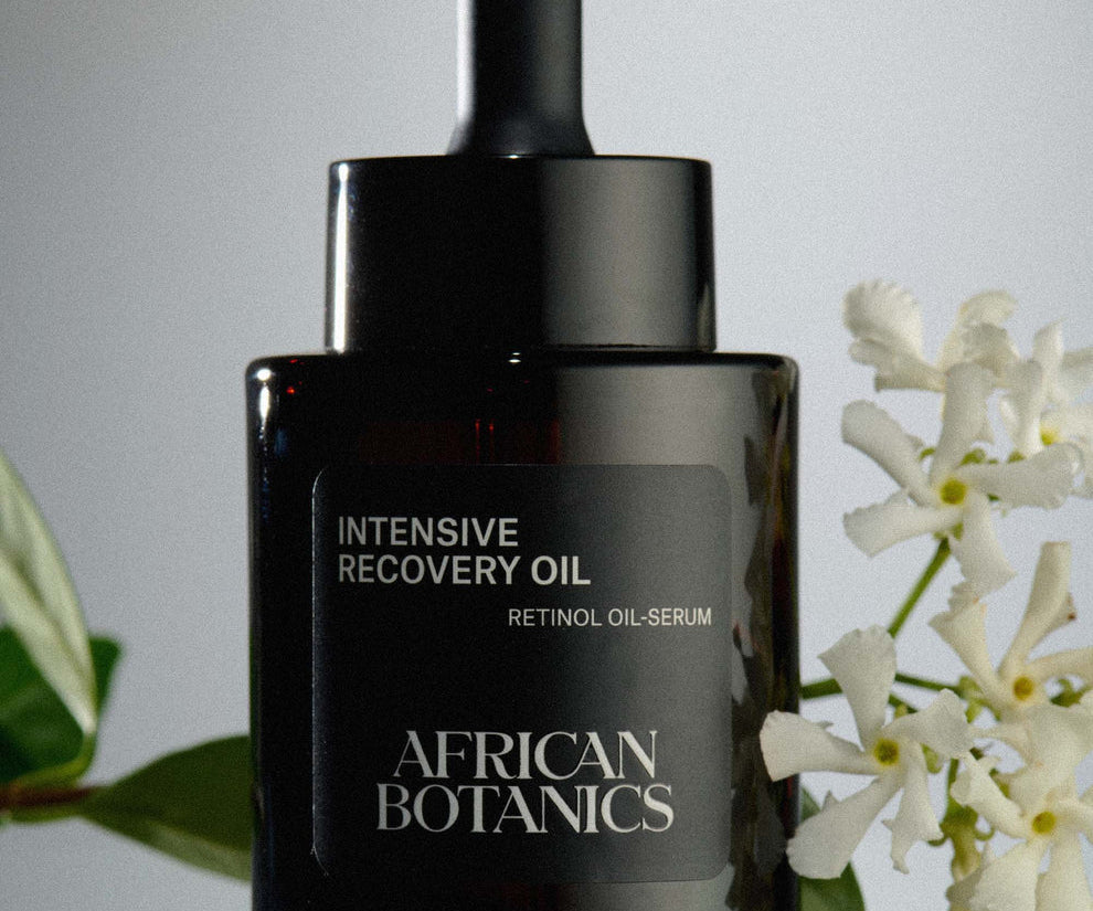 African Botanics Intensive Recovery Oil on a table surrounded by flowers.