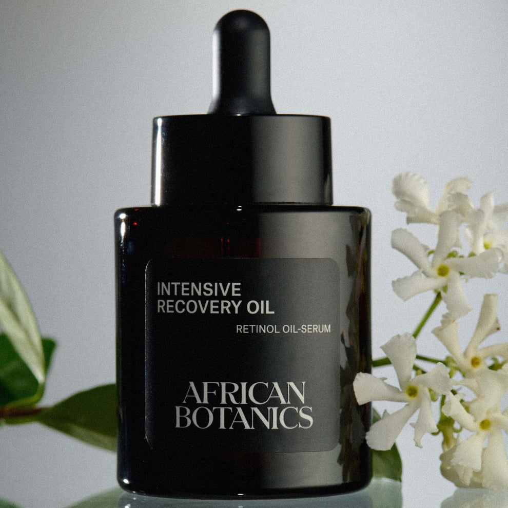 African Botanics Intensive Recovery Oil on a table surrounded by flowers.