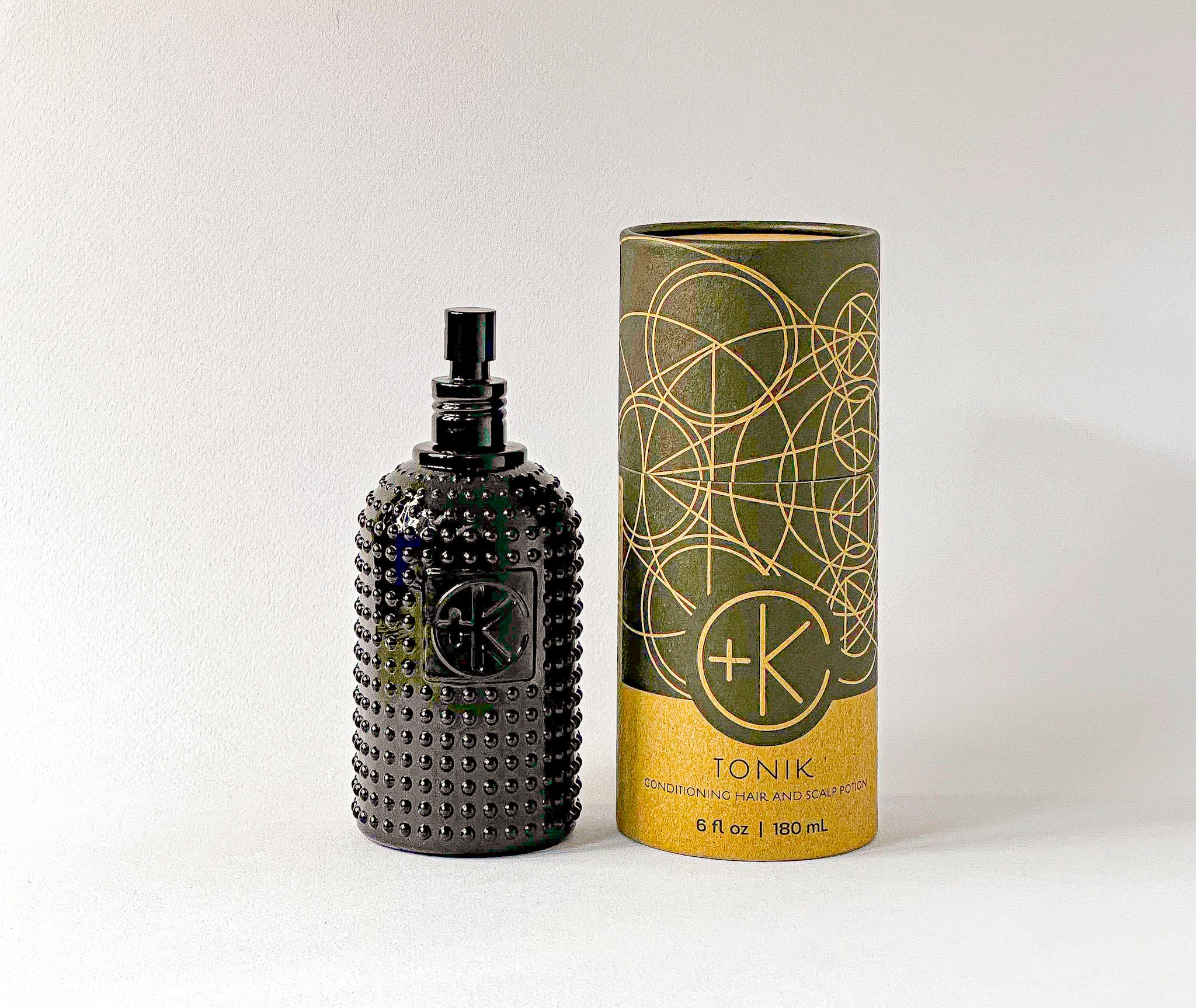 Textured black glass bottle of Cult+King TONIK with an atomizer top, beside its cylindrical cardboard and black box.