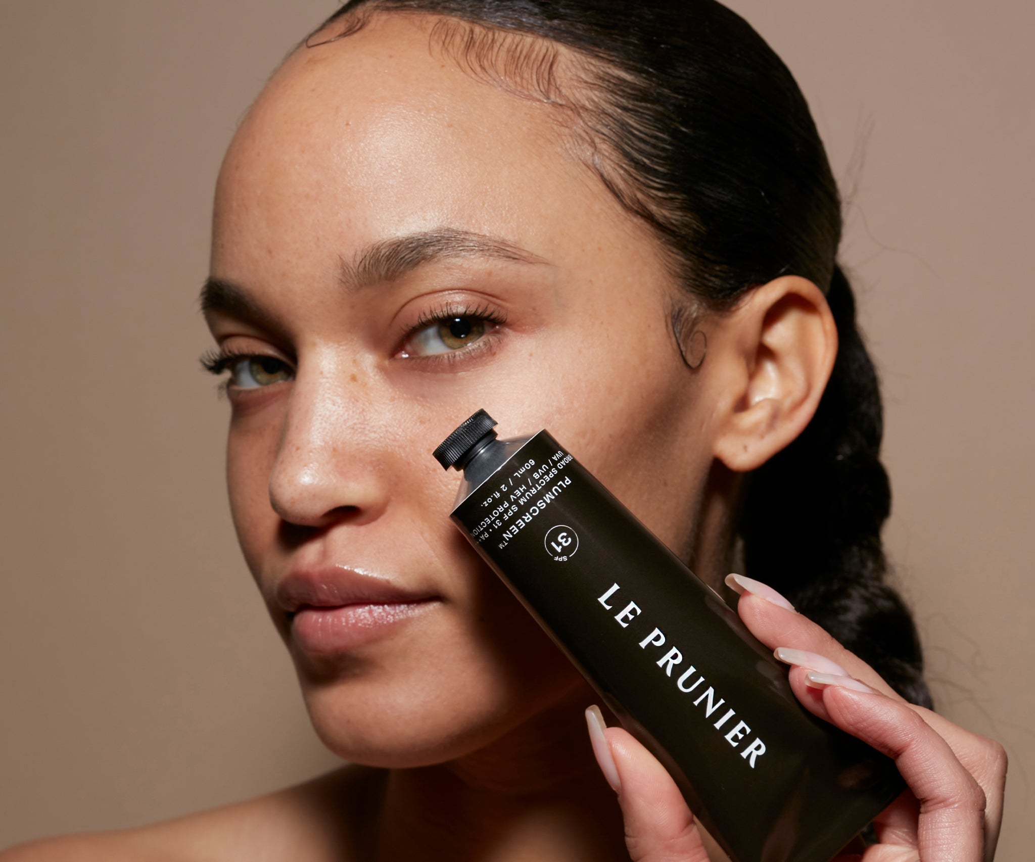 Le Prunier Plumscreen SPF 31+++ tube next to a woman's face for size comparison.
