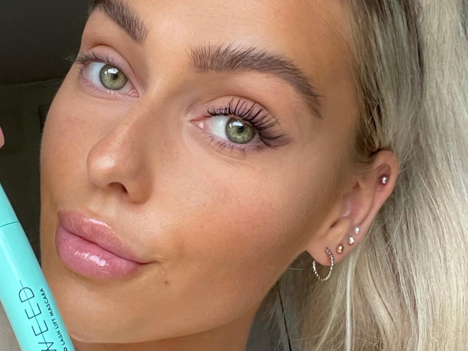 A selfie of a woman holding SWEED Pro Lash Lift Mascara, showing her long, defined lashes.