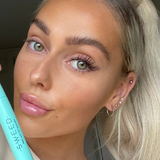 A selfie of a woman holding SWEED Pro Lash Lift Mascara, showing her long, defined lashes.