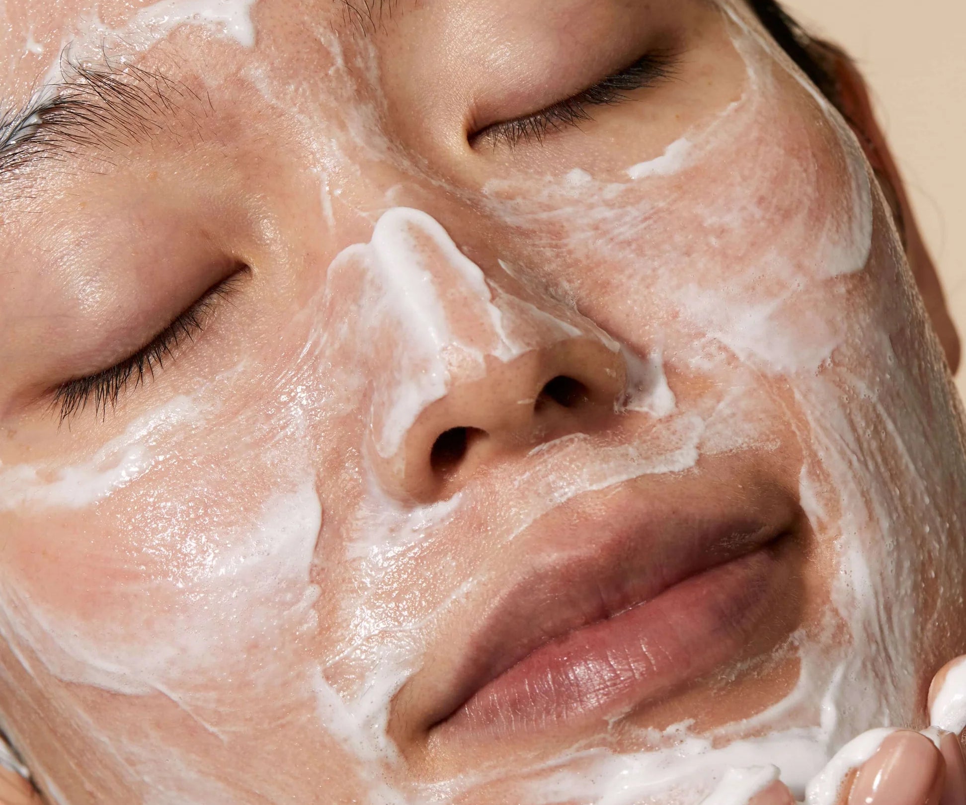 A woman with her eyes closed, covering her face in Omorovicza Cleansing Foam with her hands.