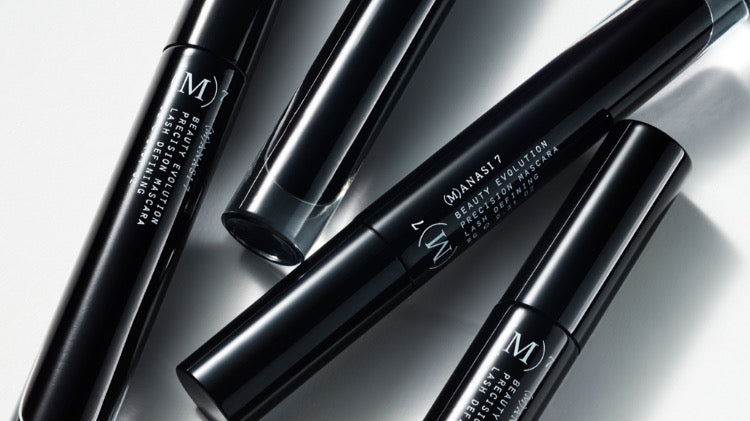 A grouping of Manasi 7 Obsidian Mascaras in a black glass tube with white branding text and a screw-on mascara wand top.