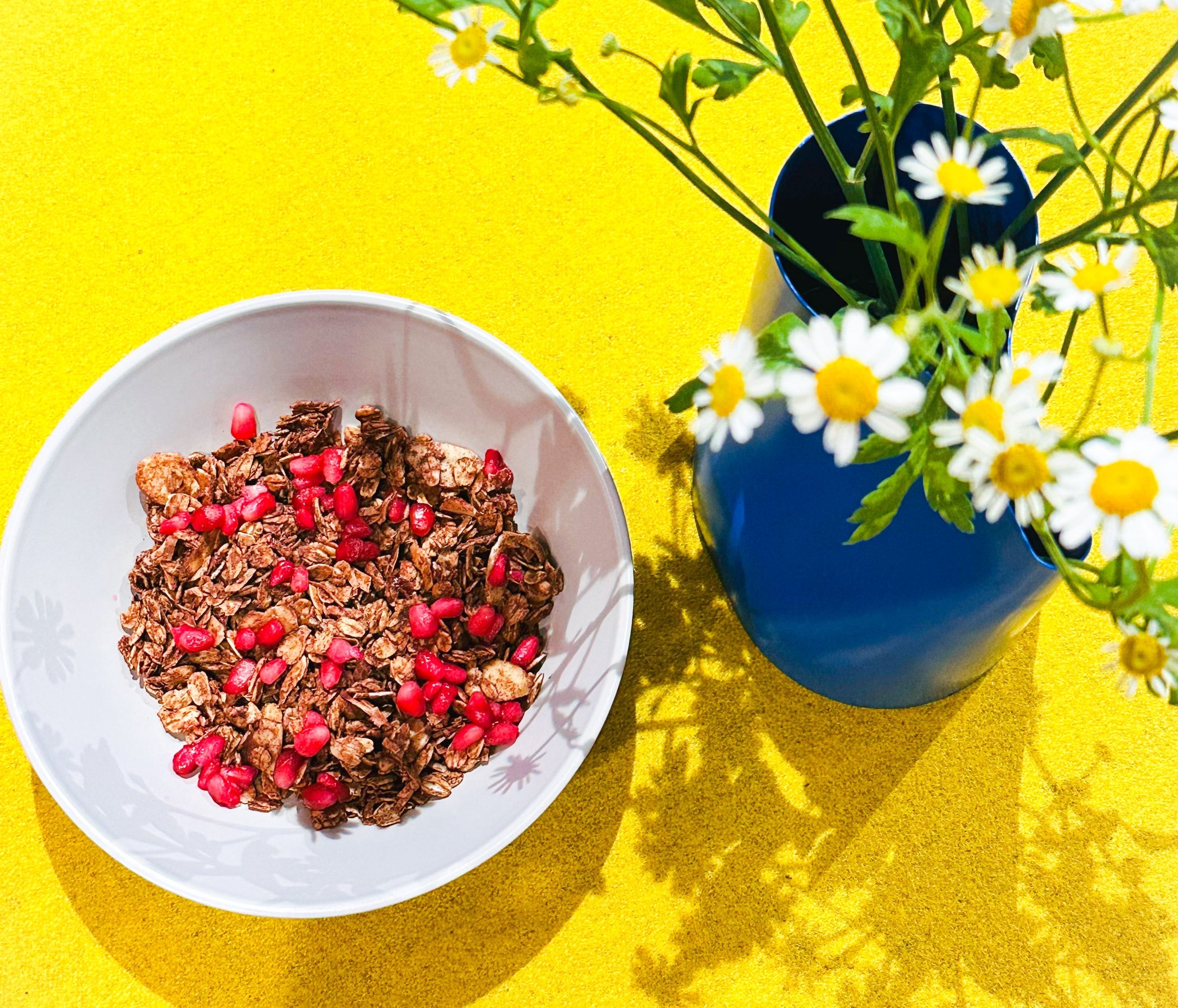 
  
  granola with pomogranate with flowers next to the bowl.
  
