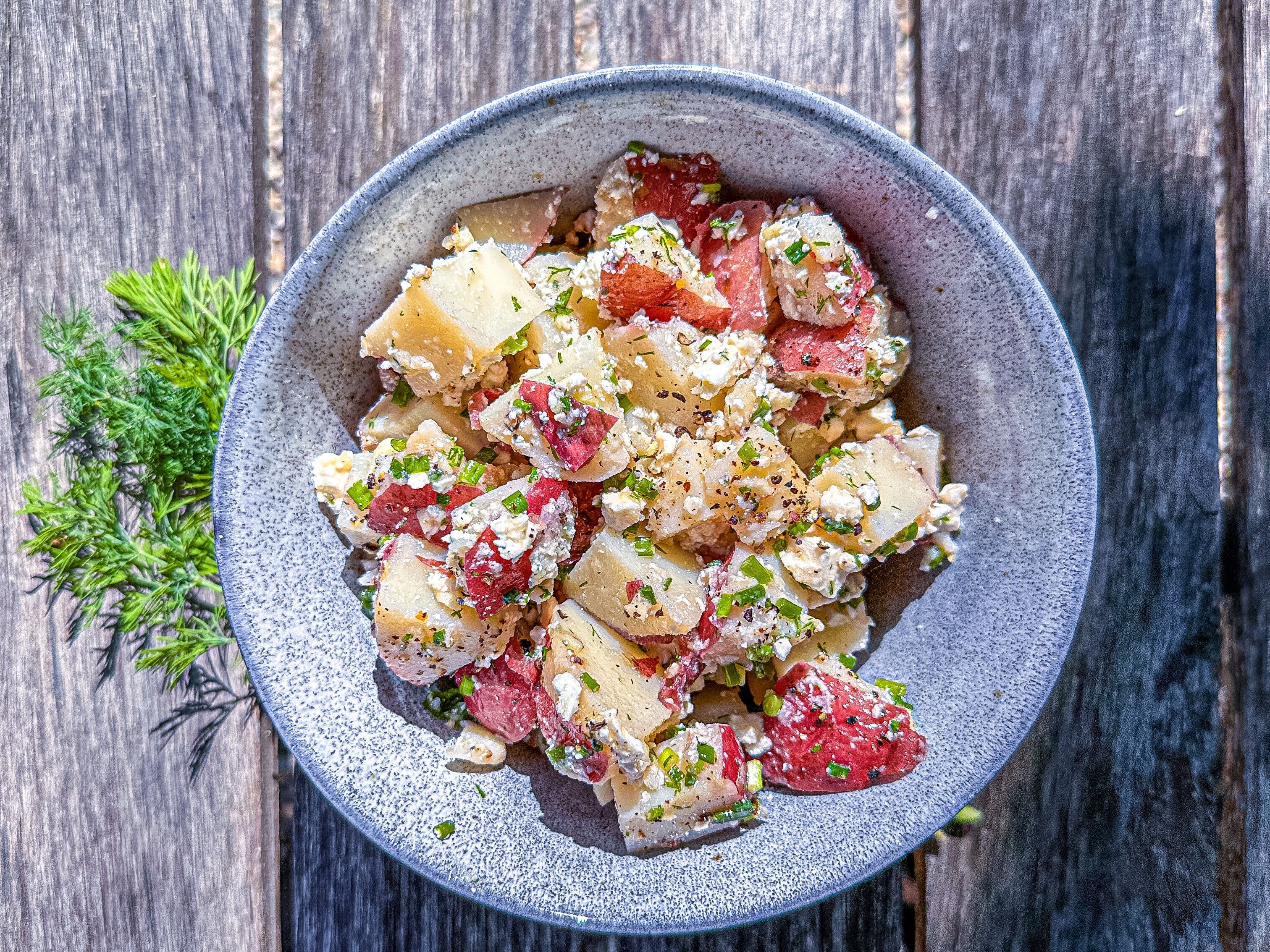 
  
  Potato Salad with fresh dill, chives and feta on a wooden bench.
  
