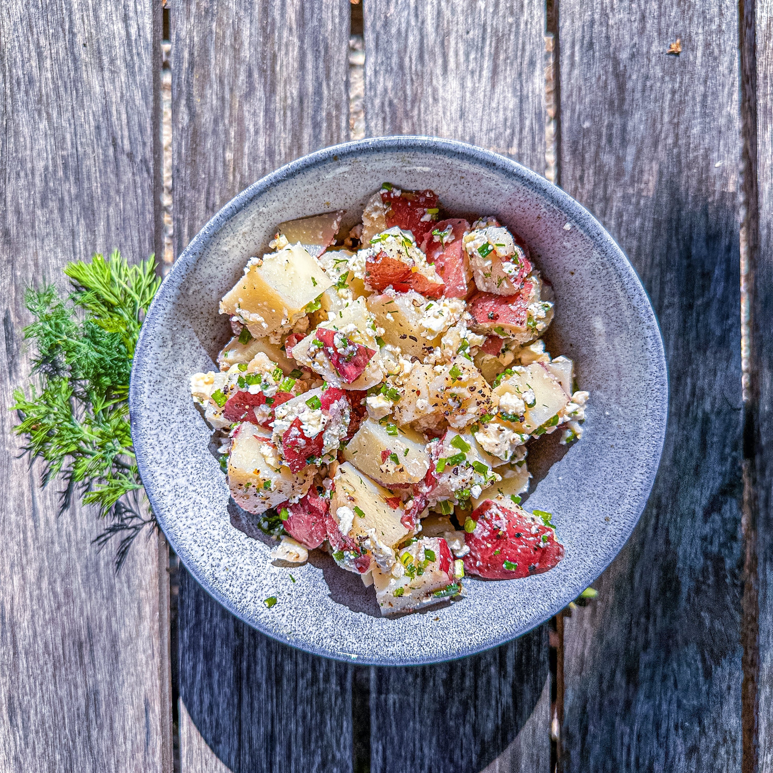 
  
  Potato Salad with fresh dill, chives and feta on a wooden bench.
  
