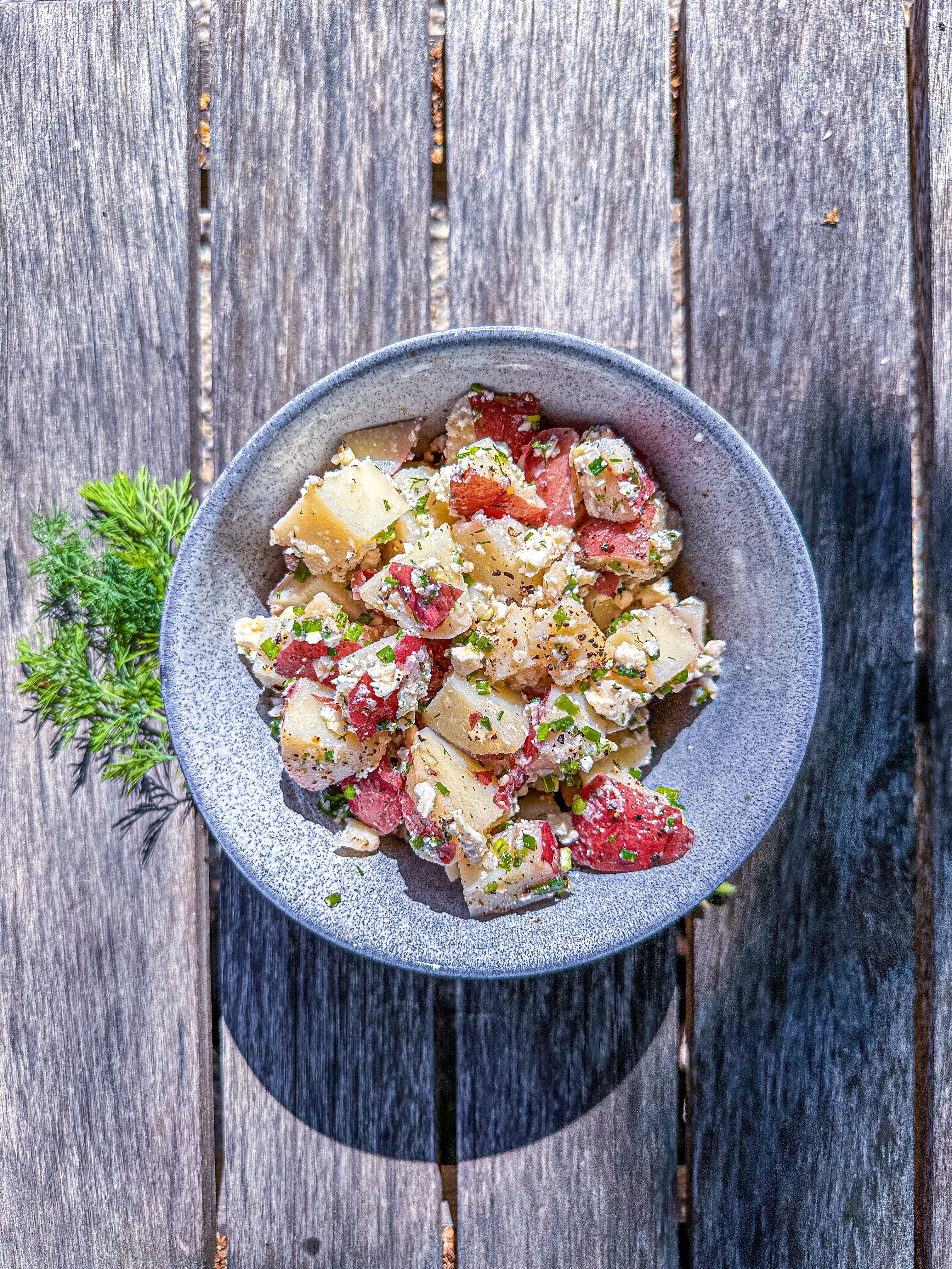 Potato Salad with fresh dill, chives and feta on a wooden bench.