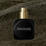 
  
  Black Osmé Fragrance Obsidian perfume bottle on sand with cap off
  
