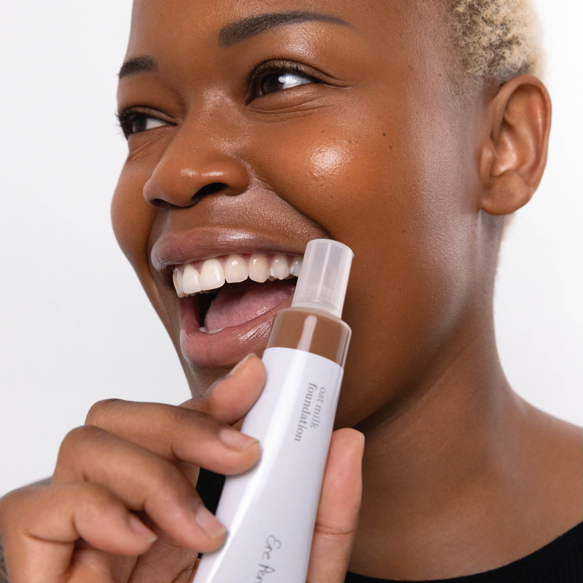 
  
  Ere Perez Oat Milk Foundation Mocha on a woman with dark complexion and neutral undertones holding Ere Perez Oatmilk Foundation.
  
