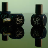 
  
  Osmé Fragrances displayed black perfume bottles with caps on and off with a green back ground and mirrored counter showing reflection.
  
