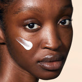 
  
  A close-up view of a woman with a swatch of Omorovicza Balancing Moisturizer on her cheek.
  
