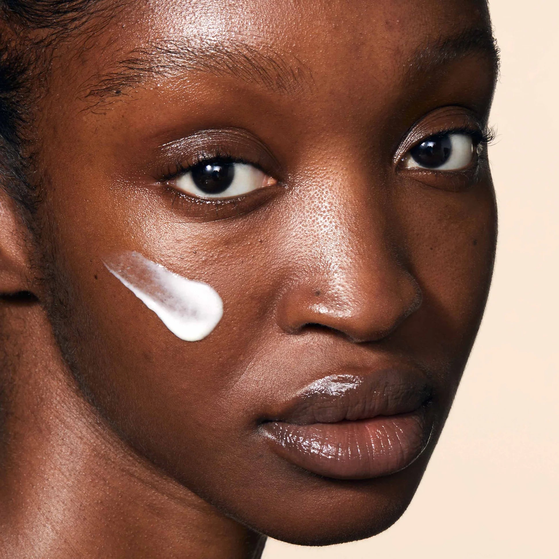 
  
  A close-up view of a woman with a swatch of Omorovicza Balancing Moisturizer on her cheek.
  
