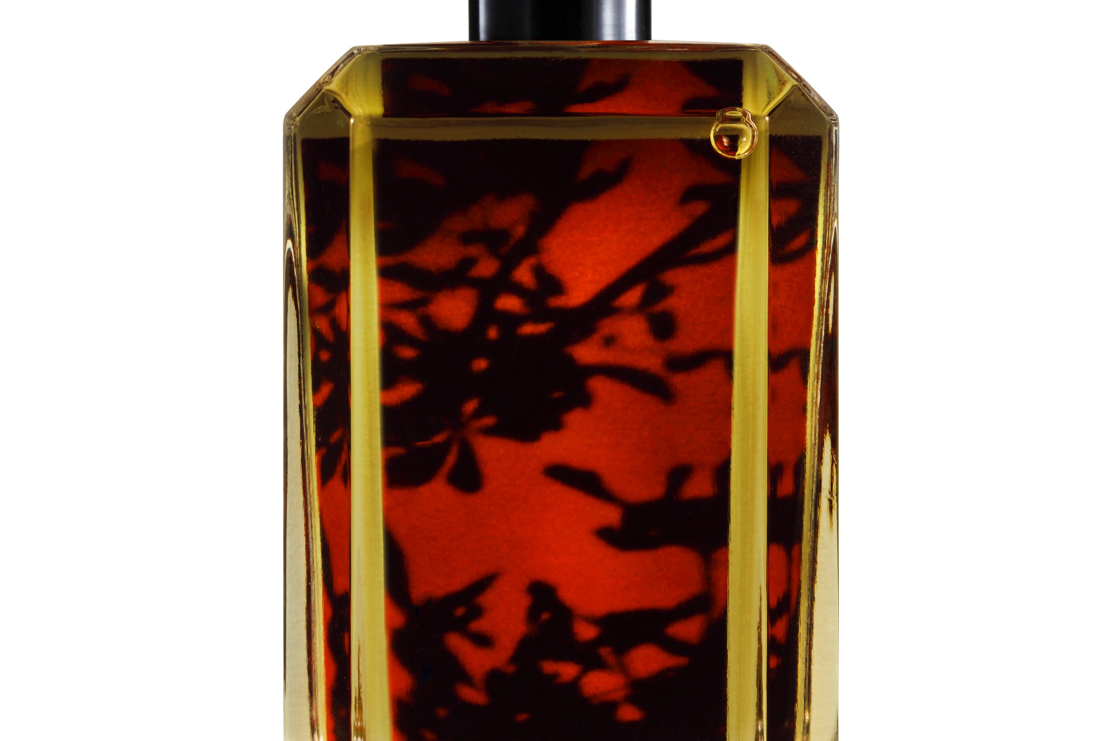 
  
  perfume bottle showing its liquid with red floral backdrop behind the logo sticker.
  
