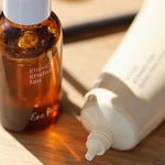 
  
  Brown bottle labeled 'guava gradual tan' and  tube of Ere Perez Moringa All Beauty Cream on a wooden surface
  
