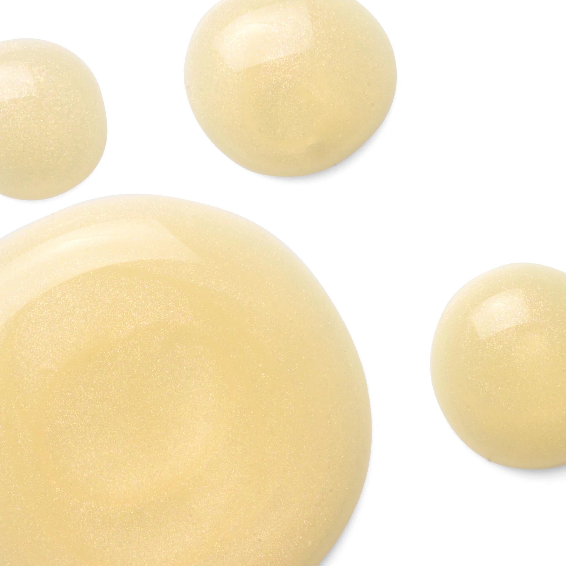 
  
  Close-up of Omorovicza Gold Flash Firming Serum with a soft, creamy texture and light yellow color, displayed in shiny droplets.
  
