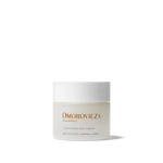 
  
  Omorovicza Cushioning Day Cream comes in a frosted glass compact jar with black branding text and a white screw-on top.
  
