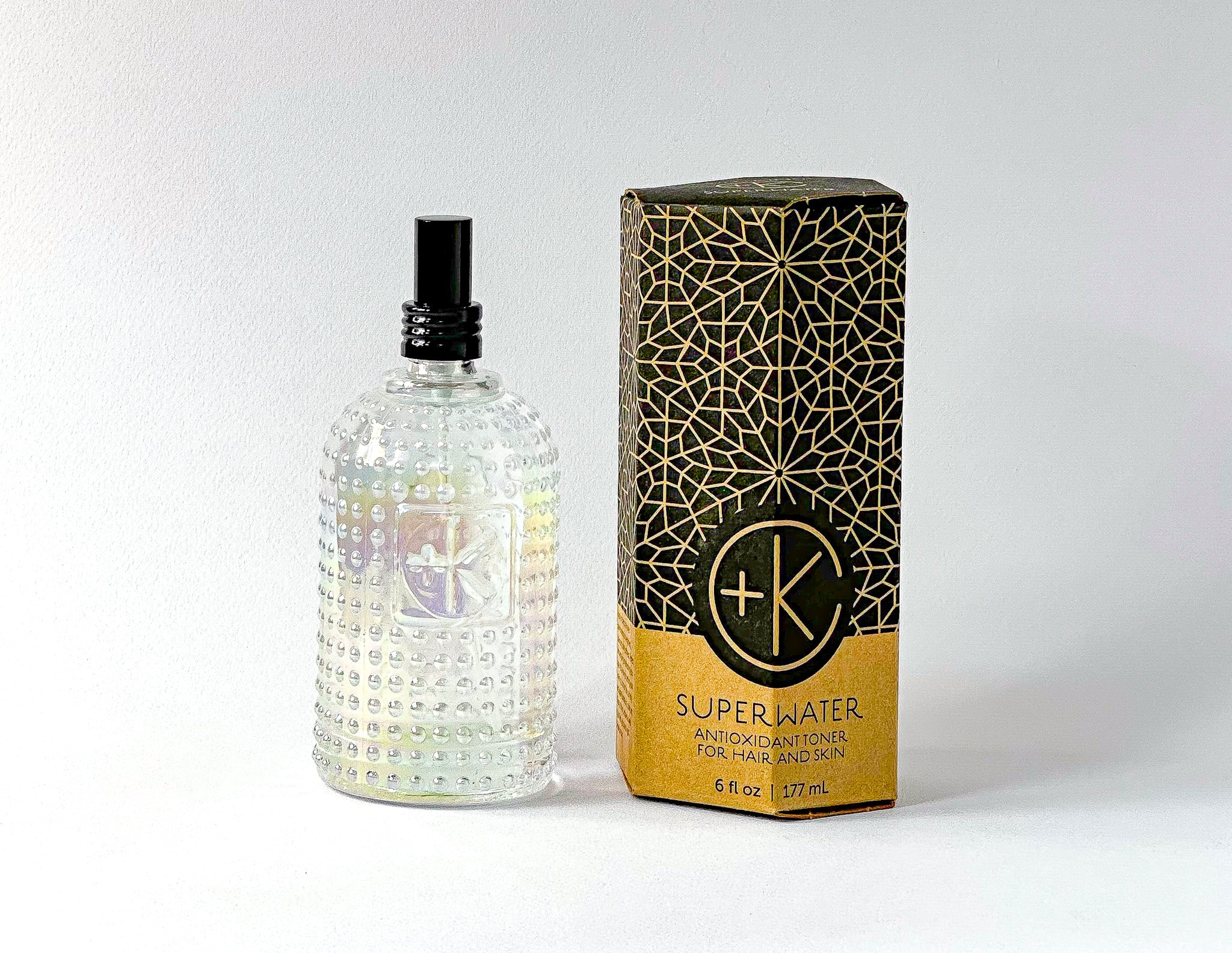 
  
  Textured glass bottle of Cult + King SUPERWATER Toner with black atomizer, beside its hexagonal cardboard and black box.
  
