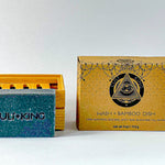 
  
  The textured Cult + King Shampoo Bar and slatted bamboo dish beside the set's geometrically patterned cardboard package.
  
