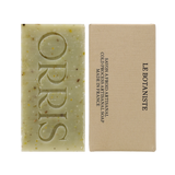
  
  ORRIS Le Botaniste green speckled Botanical Face + Body Cleansing Bar with embossed logo, next to a tan box with black text
  
